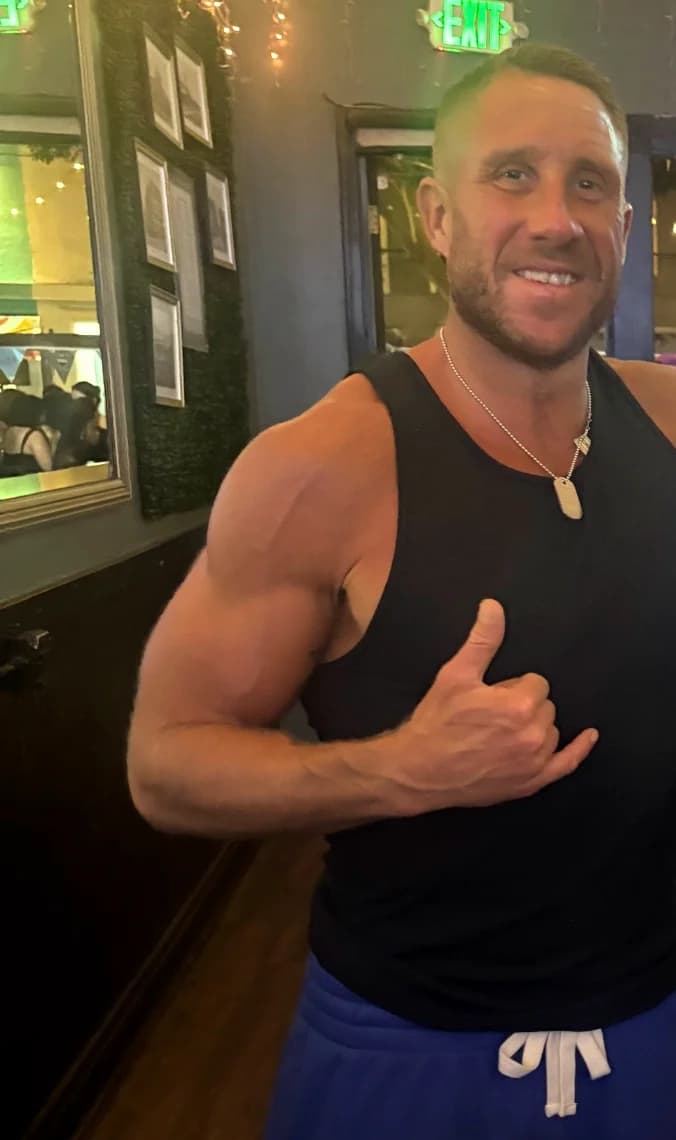 Garrett Hess in a black tank top giving a shaka sign